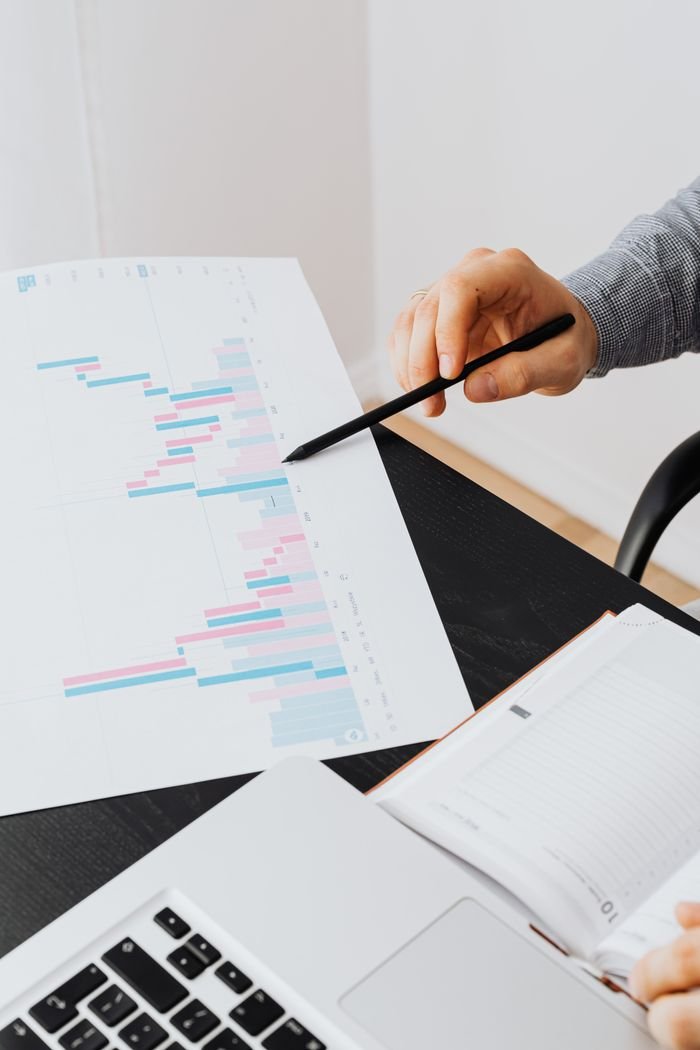 Home A professional analyzing data charts on paper with a laptop in an office setting.