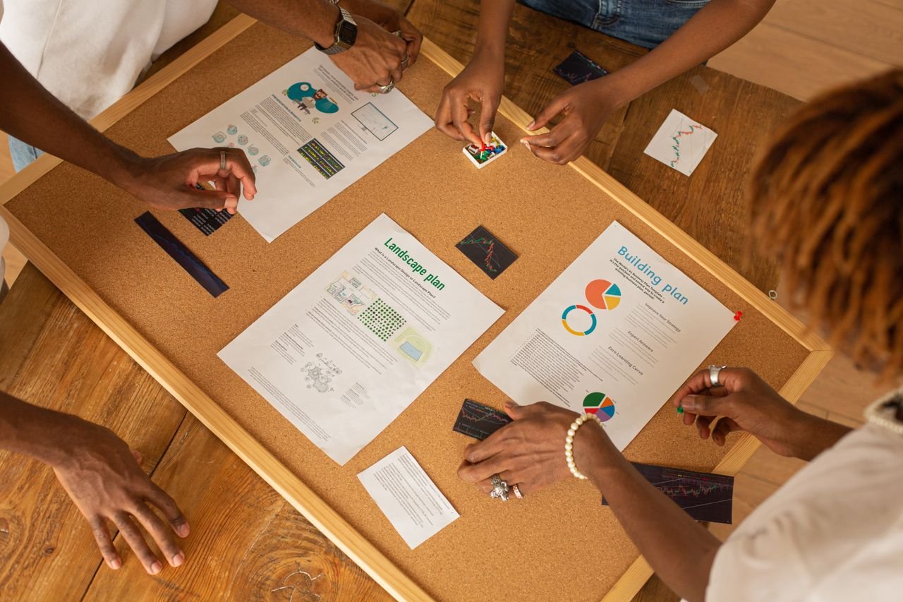 A diverse team collaborates on a workspace board with charts and plans.